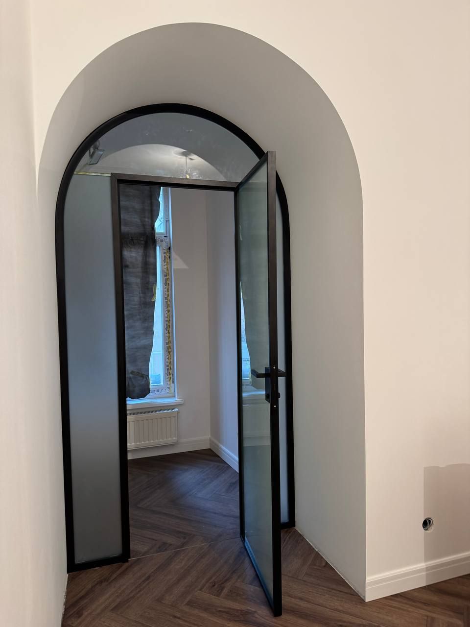 Arched glass partition with a dark profile and a door in an apartment